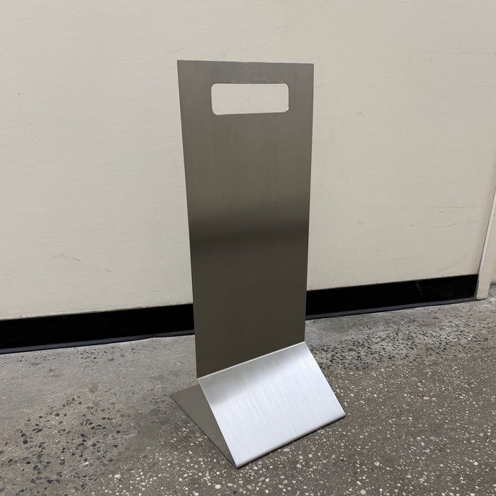 Angled view of a stainless steel floor sign showing its handle cutout and base.