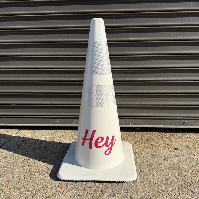 White traffic cone with pink Hey lettering and reflective bands.