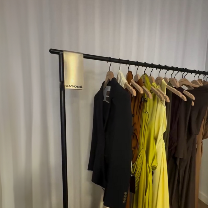 Metal sign clip on a clothing rack displaying dark and colorful garments.