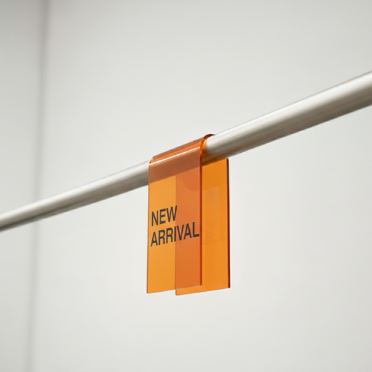 Transparent amber acrylic clothing rack clip with New Arrival lettering on a rail.