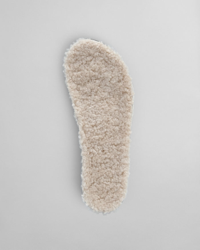 Cream-colored shearling insole with fluffy wool lining, shown from above on gray background.