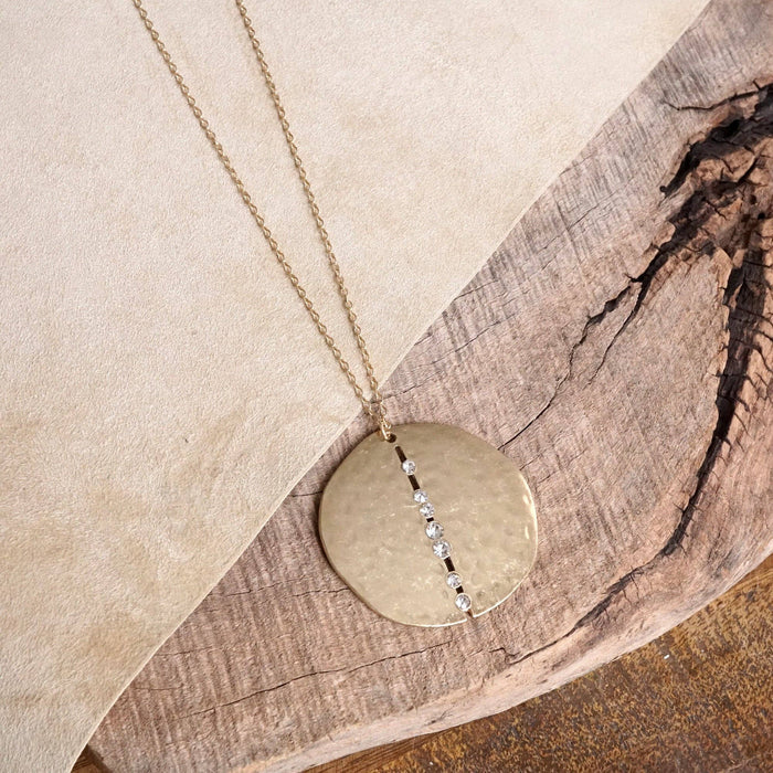 This Long Minimal Necklace features a stunning 2" round hammered disc pendant in worn gold tone, accented with multi-size clear crystals for a subtle sparkle. With its 30" length plus an extender, this versatile piece adds an elegant, understated touch to any outfit.