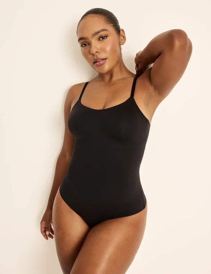 Amber is a 36C, has 46” hips, is 5’10.5” tall and wears a size L | Front view of model wearing the Customizable Shaper Thong Bodysuit highlighting the coverage and smooth fit | Black