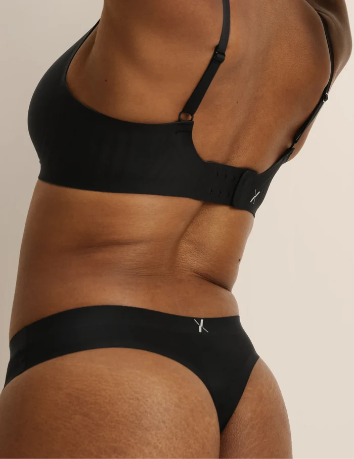 Gin has 38” hips, and wearing KNIX S | Back view of model wearing the Essential No-Show Thong highlighting the coverage and smooth fit | Black
