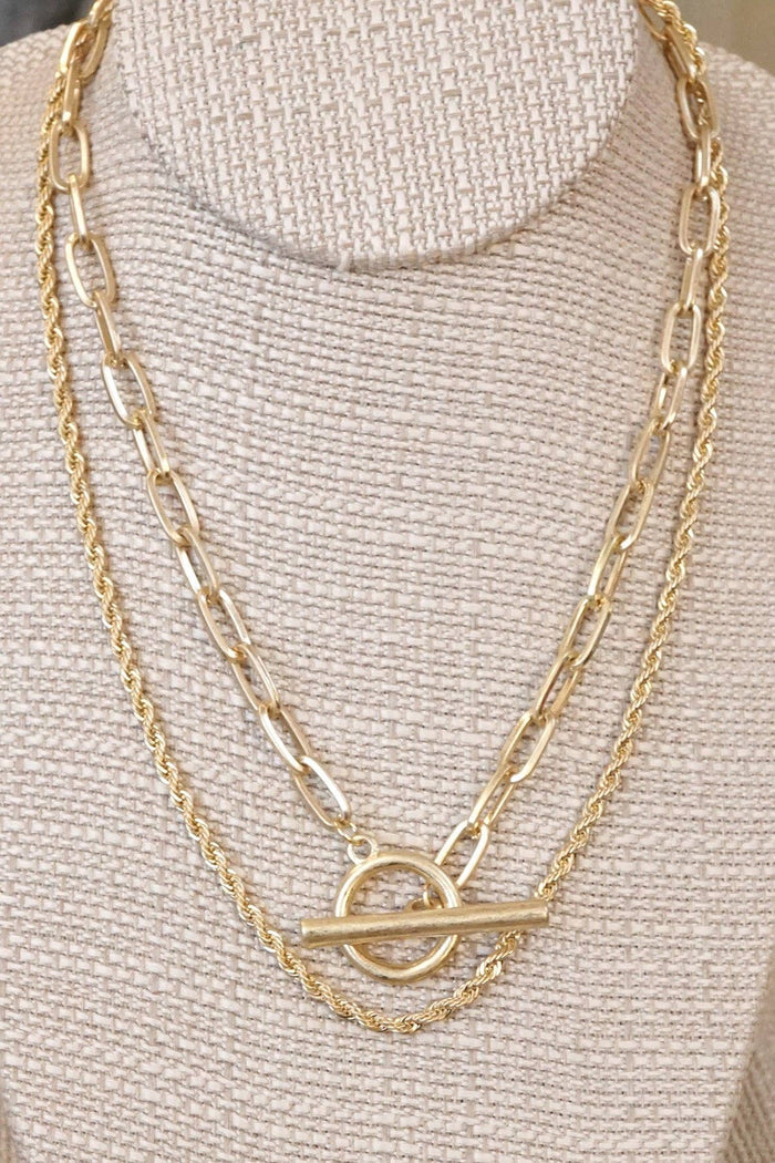 A gold-tone multi-layer chain necklace with front toggle closure and a back lobster claw closure on a mannequin.