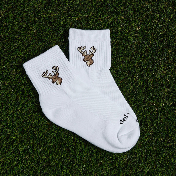 Pair of Del Campo Whitetail Deer socks with buck logo laid on grass