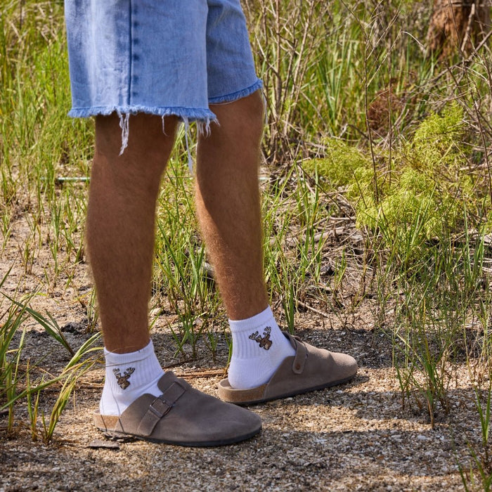 Man on a gravel trail wearing Del Campo Whitetail Deer socks with clogs