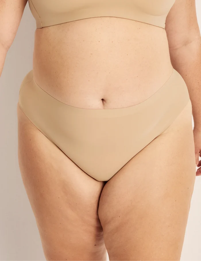 Clementine has 51” hips, and wearing KNIX XXL | Front view of model wearing the Light Leakproof No-Show French Cut highlighting the coverage and smooth fit | Warm Sand