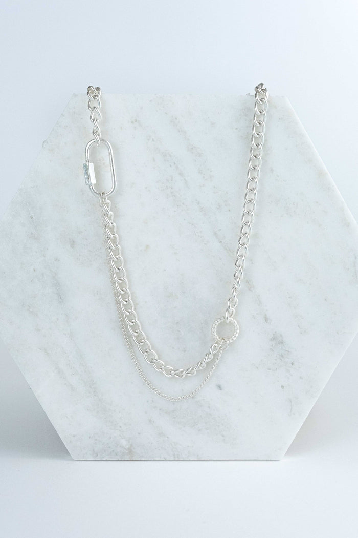 Thick, short worn silver chain necklace with a faux carabiner charm that connects a dainty silver chain to a quarter of the necklace.