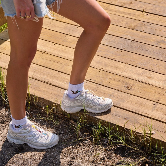 Woman stepping onto a boardwalk wearing white sneakers and Del Campo Mallard socks