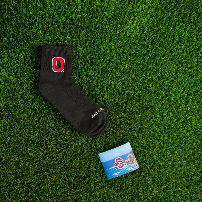 Flat lay of Del Campo Ohio State Night Mode golf socks with game-day props