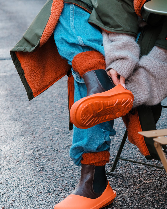 Child wearing orange rubber boots with textured sole, paired with blue jeans and orange knit socks.
