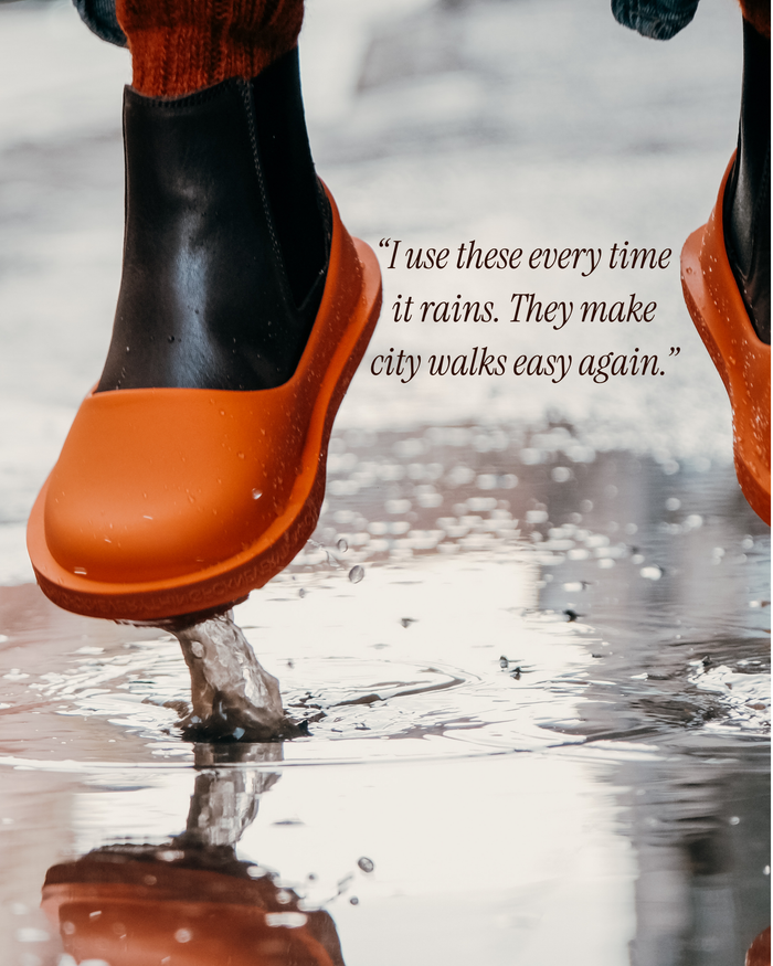 Orange and black rubber clogs splashing in a puddle during rain.