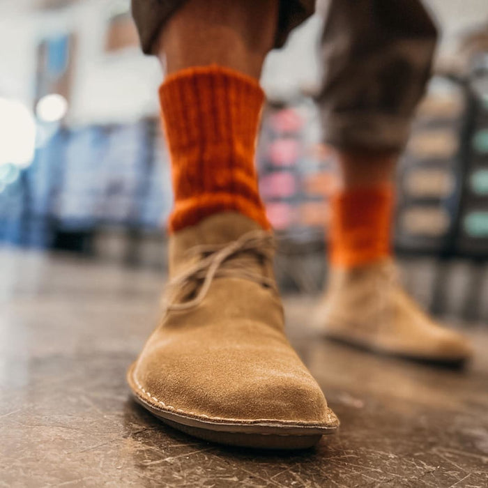 Person wearing tan suede boot with orange ribbed sock, shown from low angle view.
