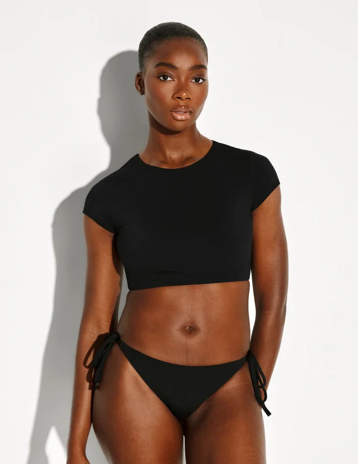 | Full-body view of model wearing the Sculpt Short Sleeve Swim Top, highlighting the neckline, sleeve design, and silhouette | Black