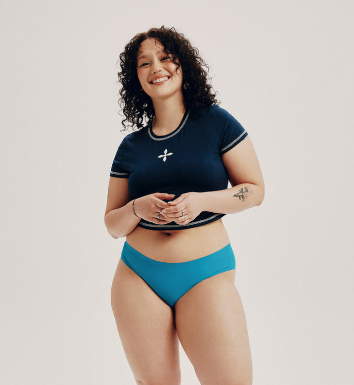 Felixe (she/her) has 44” hips and is wearing a size XL  | Front view of model wearing the Teen Light Leakproof No-Show Bikini highlighting the coverage and smooth fit | Poolside
