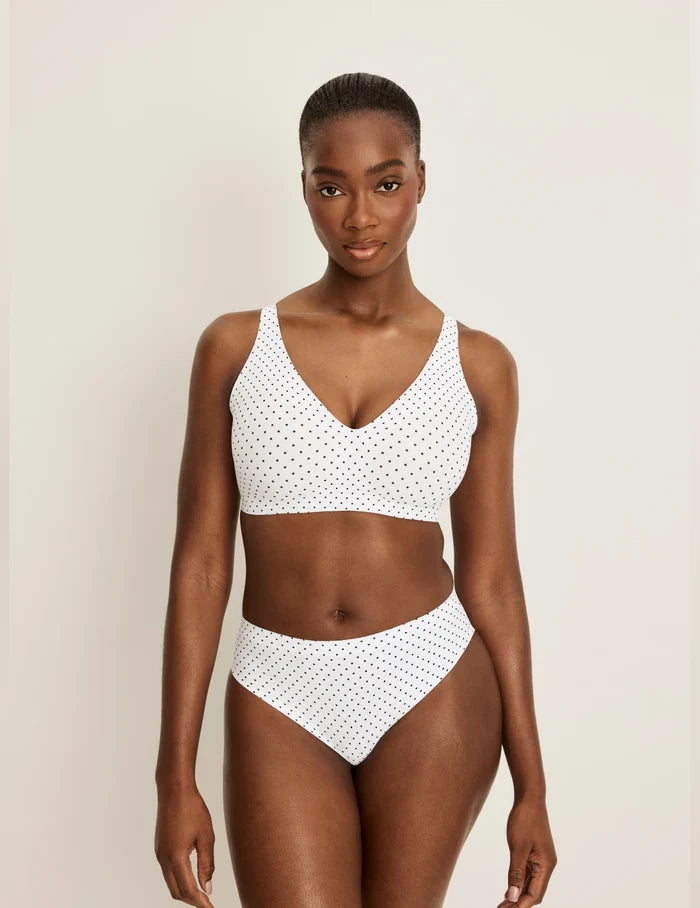 Orlane is a 32DD and wearing KNIX S+ | Full-body of model wearing the Revolution V-Neck Bra, highlighting the neckline, strap design, and smooth silhouette | White with Black Polka Dot