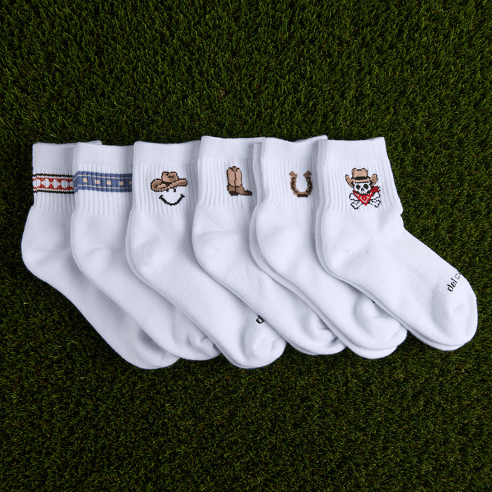 Del Campo Western Pack socks laid on golf-course turf, showing all six western designs on white crew socks.