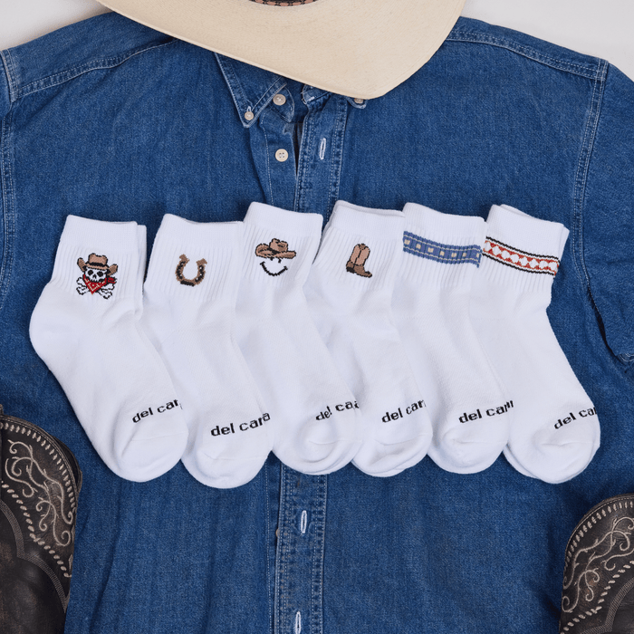 Del Campo Western Pack socks arranged on a denim shirt with a cowboy hat, showing all six western designs.